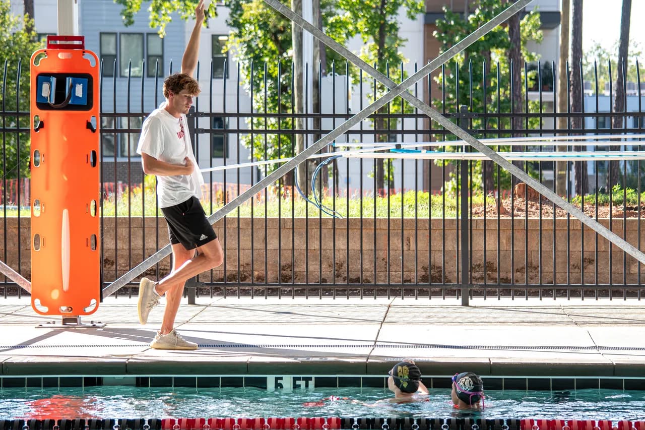Quintin McCarty stands beside the outdoor pool, observing swimmers during a Speed Force training session.
